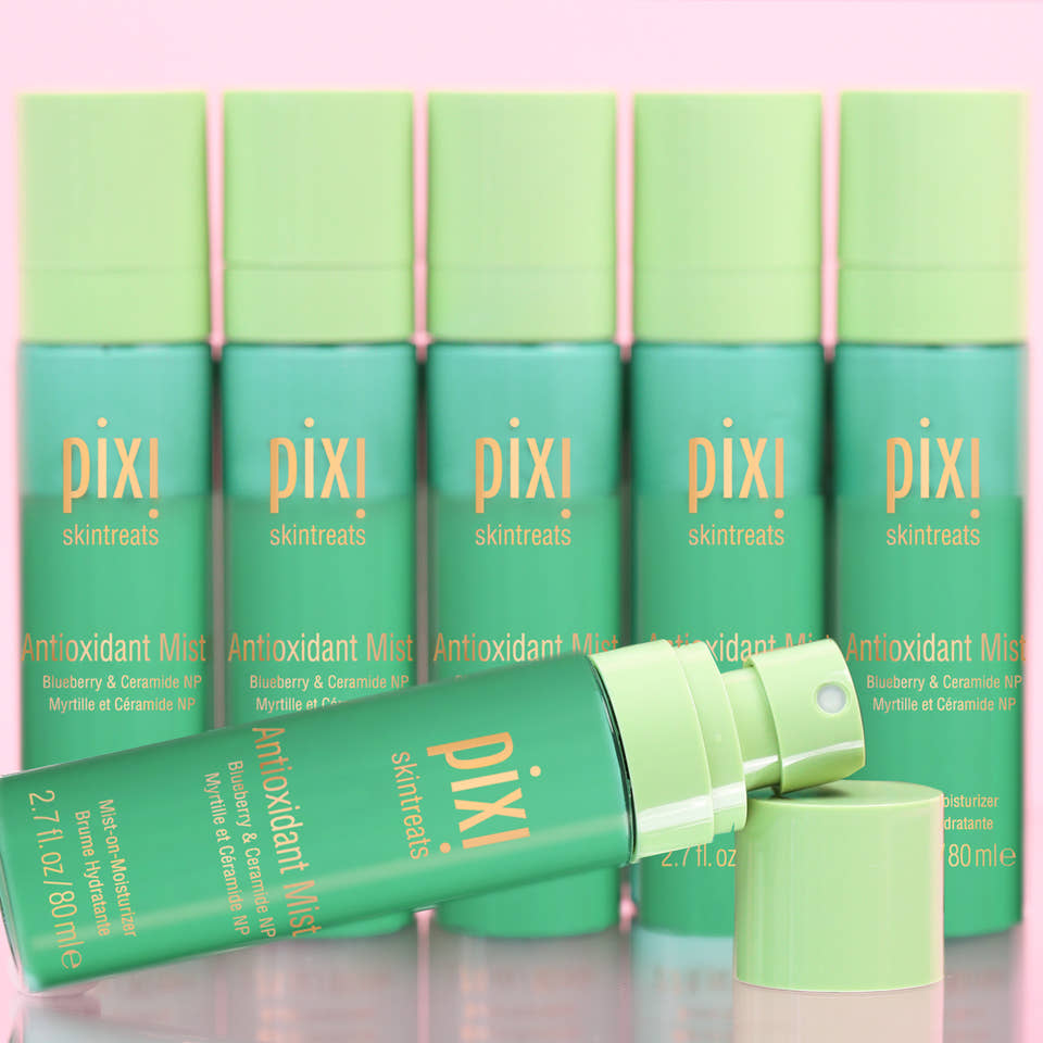 Six Pixi Skintreats Antioxidant Mist bottles in a teal and light green color scheme, with one bottle lying open in the foreground and its cap beside it, set against a soft pink background. view 1