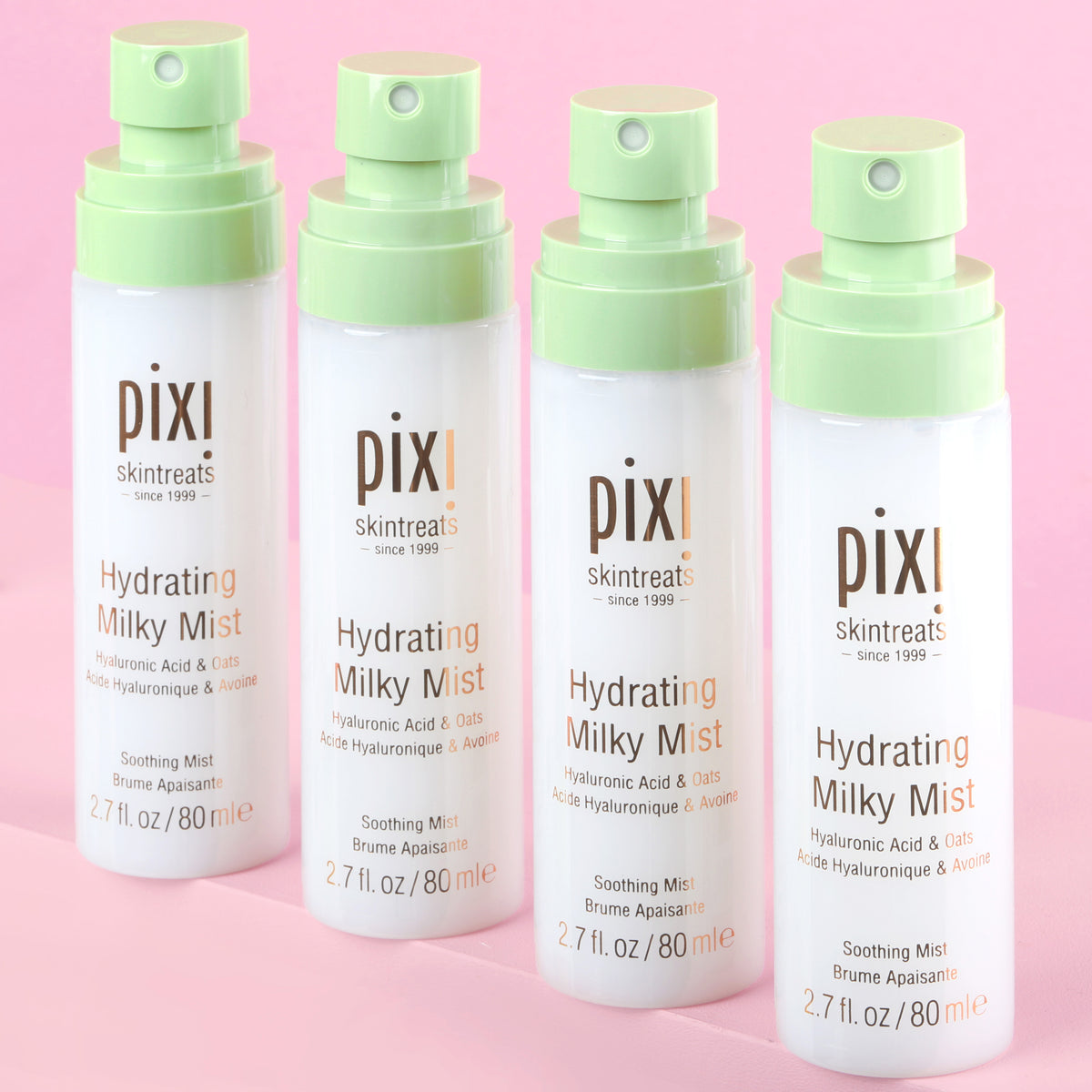 Four bottles of Pixi Hydrating Milky Mist with caps off and shown on a pink background