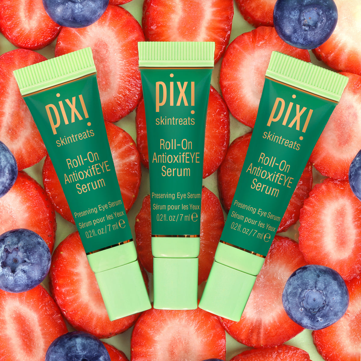 Three Pixi Roll-On Antioxidant Eye Serum bottles surrounded by strawberries and blueberries.
