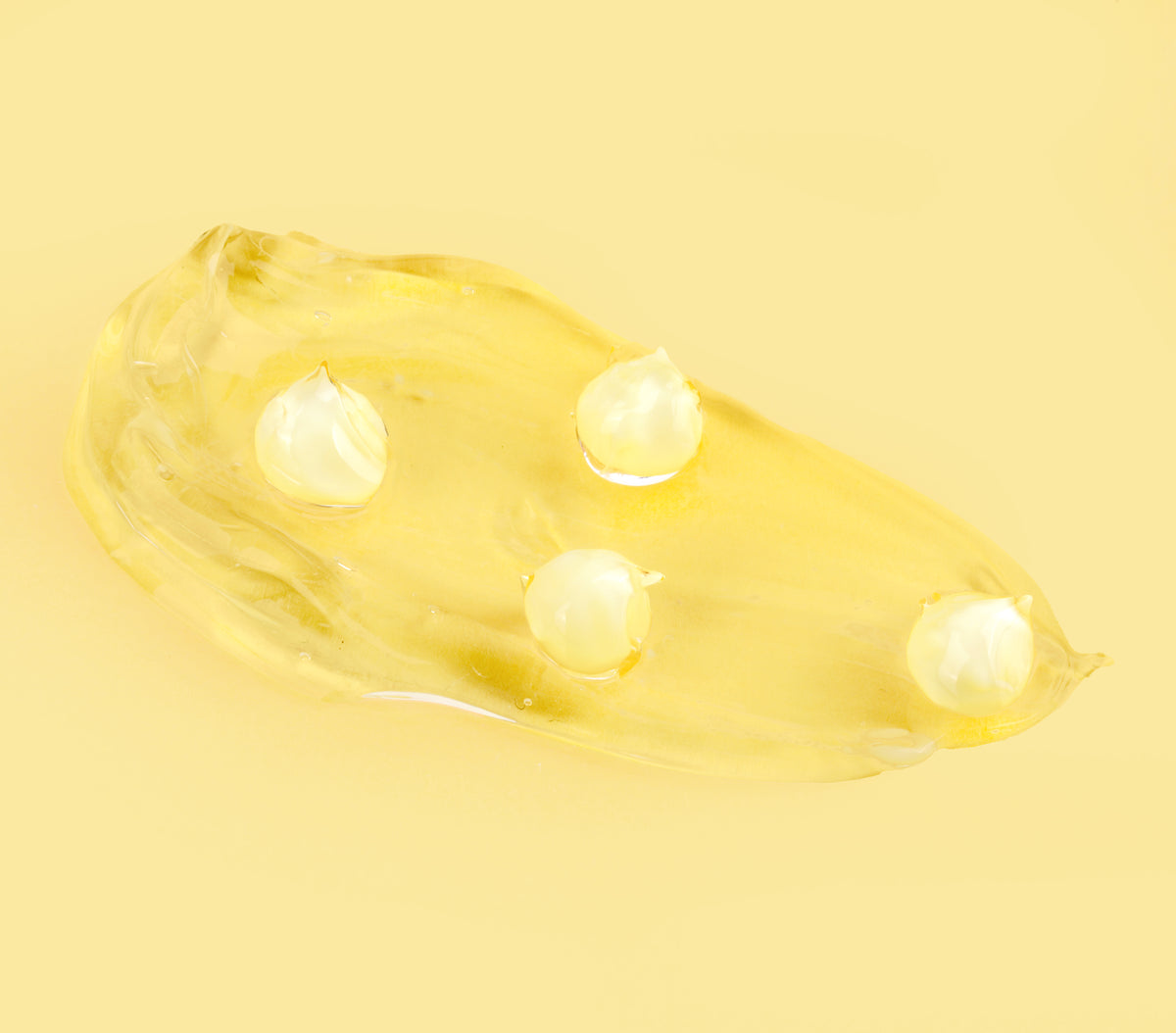 Swatch of Vitamin-C CremeSerum showing gel texture and included pearl-like moisture beads, photographed on a plain pale yellow background.